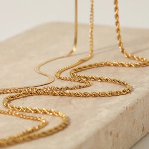 Three-layer gold stainless steel snake and rope chain necklace set on beige stone