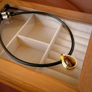 Detailed close-up of tiger eye teardrop pendant with gold bezel on luxury wooden case