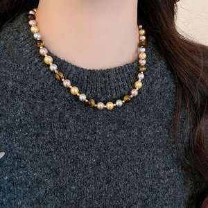 Détail d'un collier de perles œil de tigre avec accents dorés porté par un mannequin