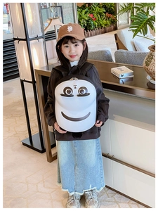Toddler girl wearing a white egg-shaped hardshell backpack with a cartoon smile pattern