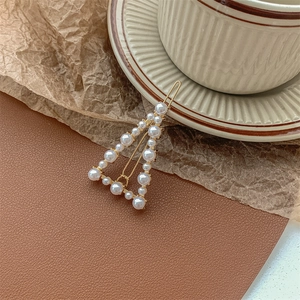Detailed close-up of a golden triangle hair clip adorned with elegant white pearls