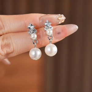 Macro shot of silver diamond-encrusted earrings with pearls held by hand to show fine details