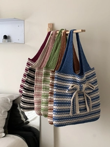 Multiple striped knit tote bags with bow detail hanging on wooden hooks in a row