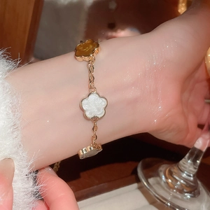 Détail d'un bracelet trèfle élégant avec des breloques en émail ambre, blanc et gris brillant