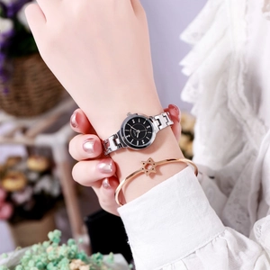 Silver steel strap watch with black dial and star charm bracelet on a female wrist