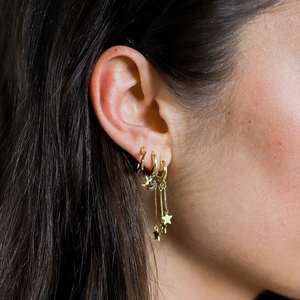 Detailed view of layered gold star and moon drop earrings on female model