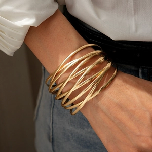 Detailaufnahme eines goldfarbenen, mehrlagigen Metallarmbands am Handgelenk eines Models
