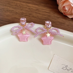 Detail of sweet bow earrings featuring pink crystals and frosted star pendants