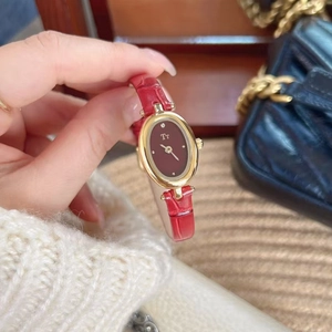 Close-up of red leather watch with oval gold case and Tt logo on woven background