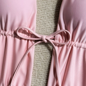 Detail of pink glossy one-piece swimsuit with drawstring bow and ruched texture