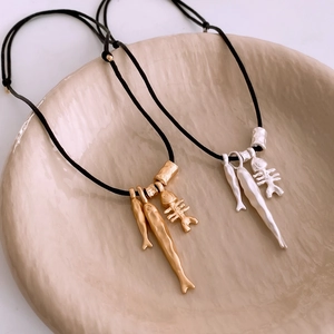 Detailed close-up of fish and bone metal pendants on a minimalist beaded necklace