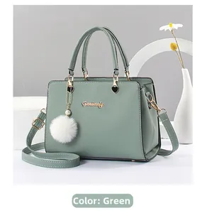 Detail of grey-green leather handbag with golden hardware logo and white fur ball charm