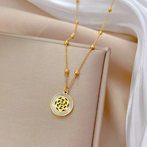 Macro detail of gold camellia shell pendant with beaded chain on soft white silk