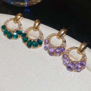 Dettaglio di eleganti orecchini d'oro con pietre color smeraldo e viola e cristalli lucenti