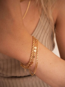 Close-up of gold layered bracelet set featuring rope, disc, and curb chains