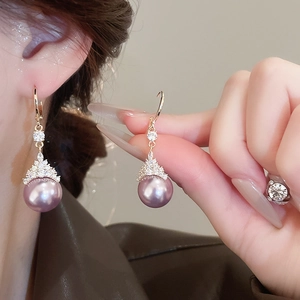Détail de boucles d'oreilles dorées avec perles violettes et zircon sur un mannequin