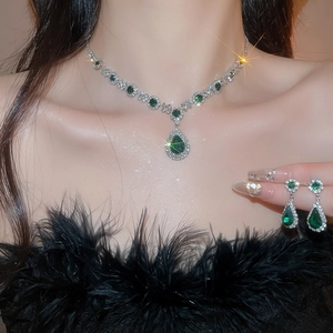 Close-up of model wearing silver necklace and earrings with green pear-shaped gemstones
