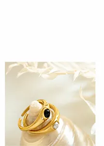 Detalle de anillo dorado ajustable con gema negra y perla sintética blanca fina