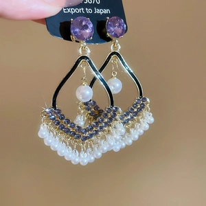 Macro view of gold-tone earrings featuring purple crystals and white pearl tassels