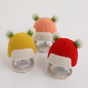 Three cute knitted baby hats with plush ear flaps and frog pom-poms for winter warmth
