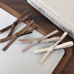 Detailed view of four leather bow hair clips in brown and beige tones on wooden tray