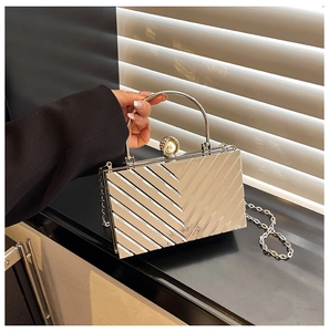 Close-up of silver acrylic clutch with V-shaped texture, pearl clasp, and metal handle
