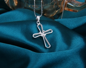 Gros plan du pendentif croix en argent avec chaîne à billes sur satin sarcelle foncé