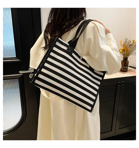 Dettaglio della grande borsa tote in tela a righe bianche e nere sulla spalla della modella