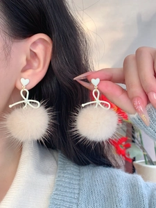 Detailed view of silver needle bow earrings with soft pink plush pompom pendant