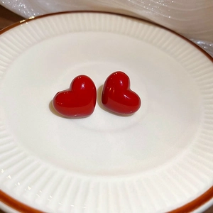 Detailed view of red heart earrings with glossy finish on a textured white porcelain plate