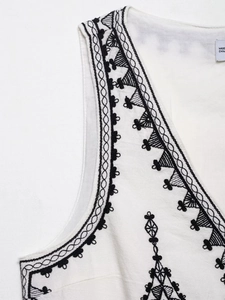 Detailed close-up of ethnic geometric embroidery on white cotton sleeveless V-neck vest