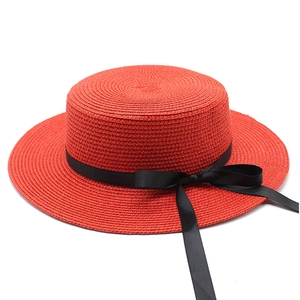 Détail d'un chapeau de paille rouge à toit plat avec texture tissée et nœud noir