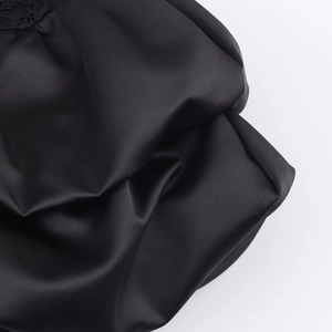 Close-up of black satin dress fabric featuring delicate lace edges and elegant pleats