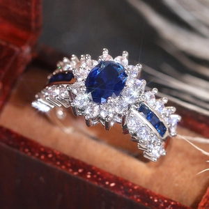 Makroaufnahme eines ovalen Saphirrings mit Diamant-Halo in einer roten Samtbox