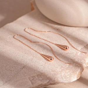 Macro shot of rose gold water drop tassel earrings on a light stone base with high polish