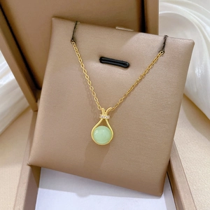 Macro view of gold necklace with green circular pendant and diamond-encrusted lucky bag detail