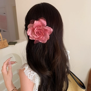 Detail of an elegant gradient pink fabric rose hair clip pinned on long wavy dark hair
