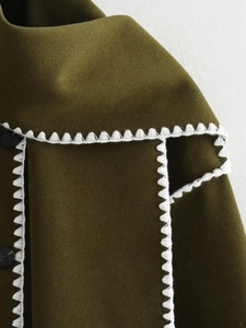 Macro detail of dark olive wool jacket with white wavy embroidery and black button