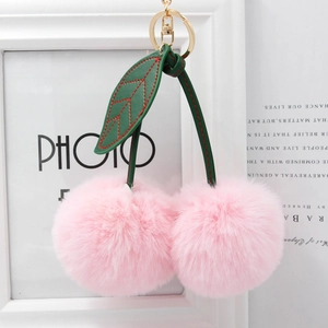 Detail of pink faux fur cherry keychain with green leather leaves and golden metal clasp
