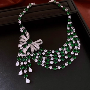 Close-up of silver bow pendant with emerald green gemstones and dangling tassels