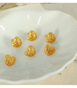 Close-up of golden heart earrings with woven texture on a white shell-shaped dish