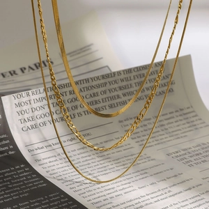 Layered gold stainless steel necklaces with snake and figaro chain styles on newspaper background