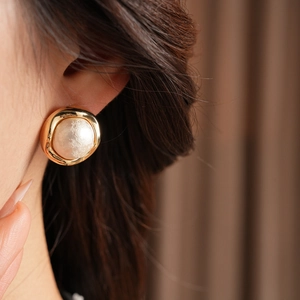 Close-up of a gold-plated vintage round button earring with a white pearl on a model