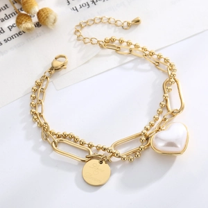 Detailed shot of double-layered gold bracelet with heart pearl and engraved Love Dream charm