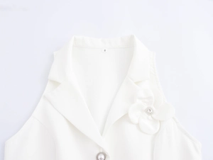 Detail view of a white sleeveless top featuring 3D floral accent and a pearl button