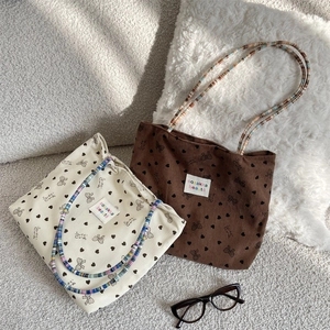 Detail view of corduroy tote bags with heart patterns and woven handles on soft background