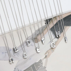 Close-up of silver bubble 26 initial letter pendants hanging on thin metal chains