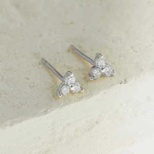 Gros plan de boucles d'oreilles en argent avec trois zircons sur fond de pierre naturelle