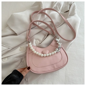 Detailed view of pink crescent bag with pearl handle and silver heart charm on a blazer