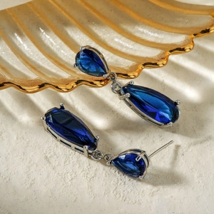 Vintage teardrop silver earrings with deep blue zircons on white sand background